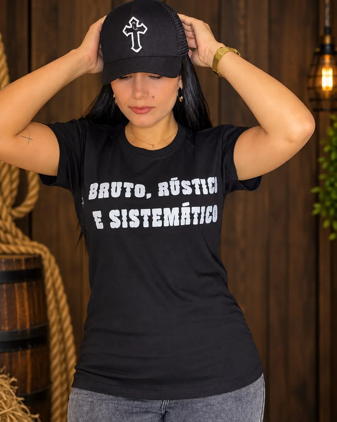 Modelo de boné preto, com as mãos na aba, com a Camiseta Bruto, Rústico e Sistemático